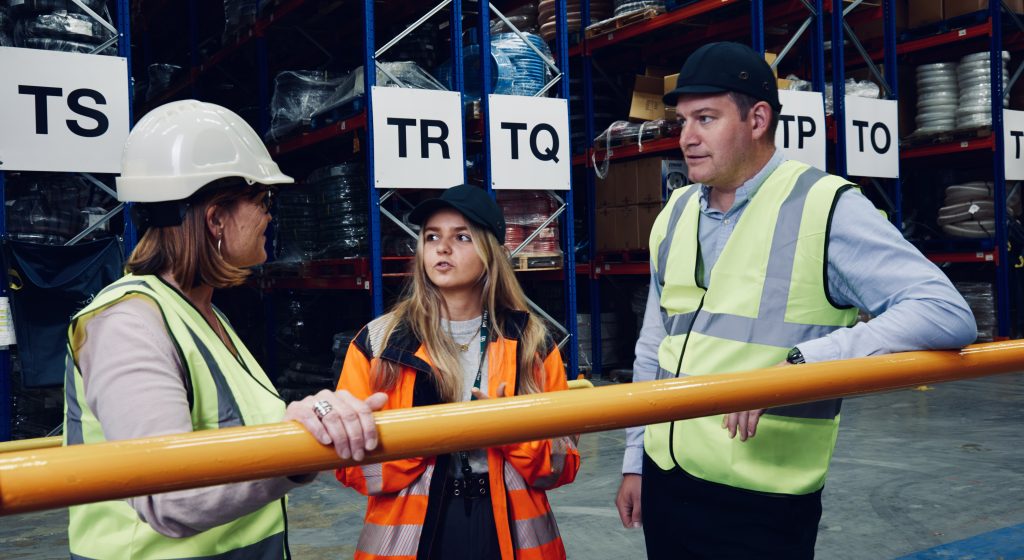 Three people having a conversation while standing in a warehouse.