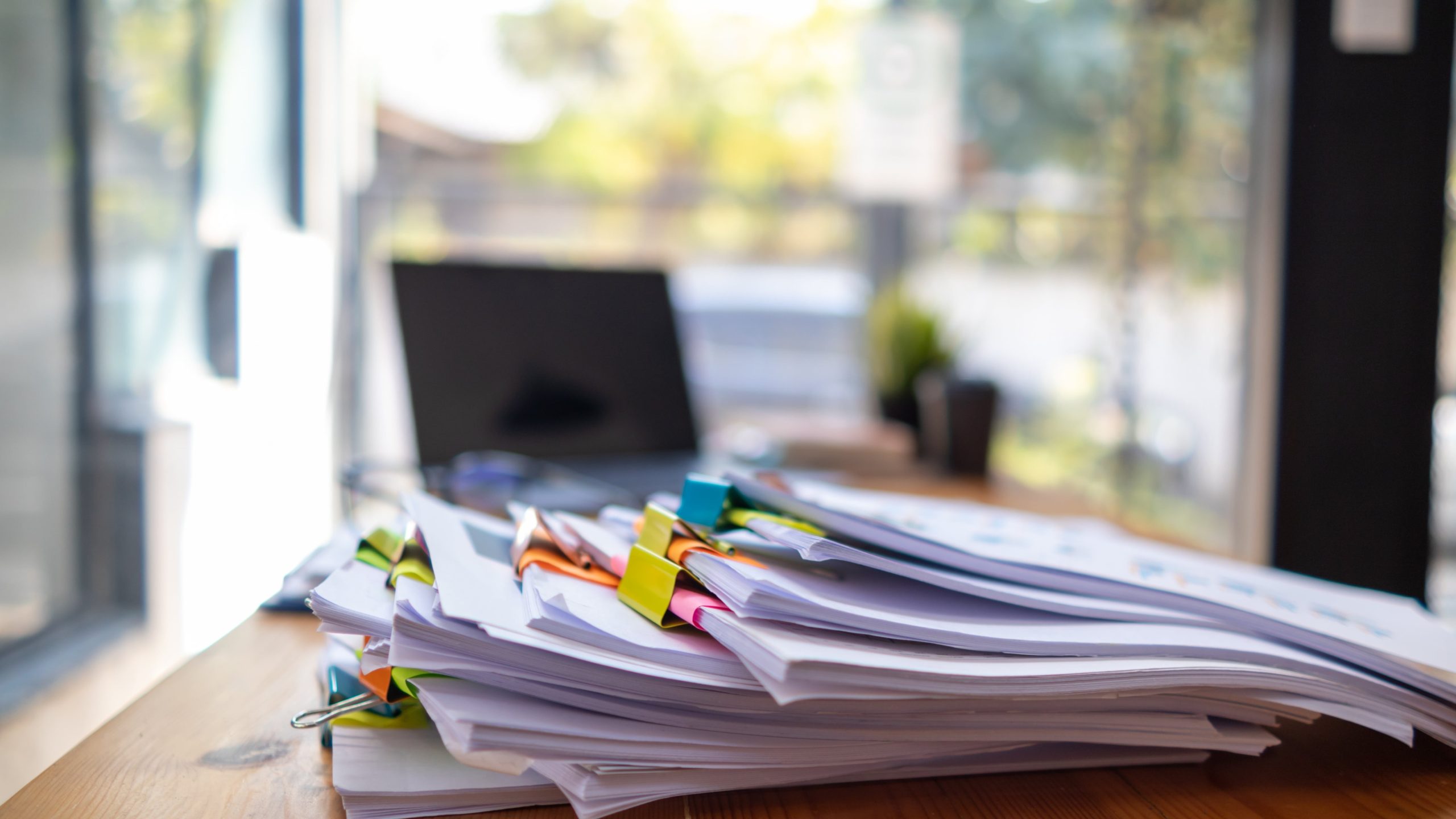 Documents held together by bulldog clips in a large stack on a desk